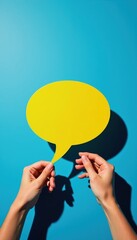 Fototapeta premium Hands hold yellow speech bubble on blue background. This symbolizes ideas, communication, dialogue, and sharing information. Use for messages, chat, or opinion graphics.