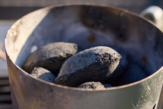 Charcoal briquettes sit inside a metal chimney starter for a grill