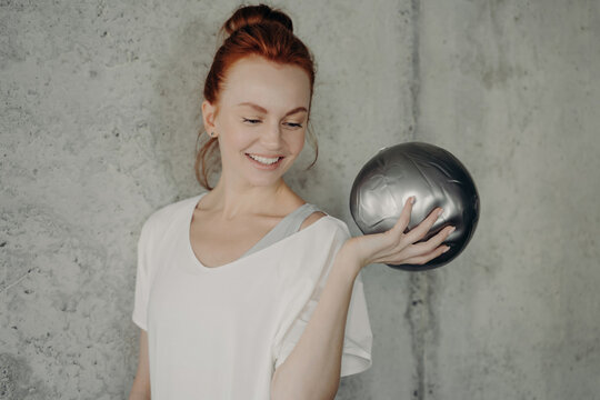 Smiling fitness woman holding small exercise ball in gym studio