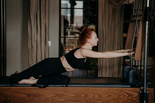 Woman doing Pilates on reformer machine in studio stretching during fitness workout session