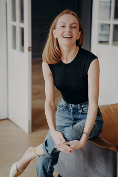 Smiling young woman sitting at home in casual clothes looking at camera