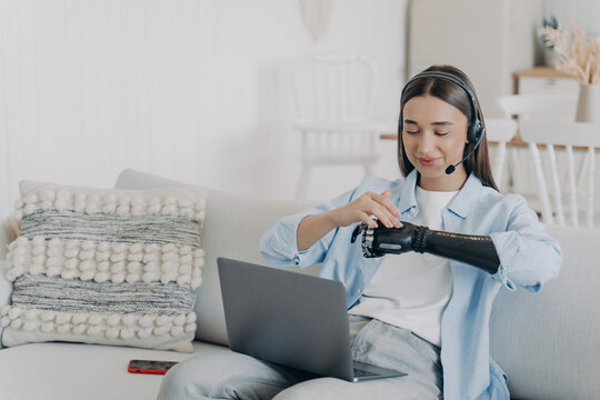 Disabled woman with prosthetic arm working on laptop from home with headset