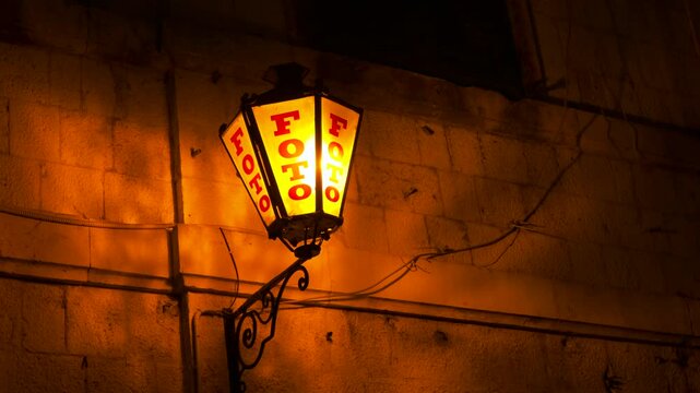 Vintage glowing orange photo shop lantern at night. Old-fashioned street lantern with a red foto sign glowing with a warm orange light, hanging on a rustic stone wall at night