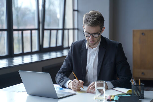 Business man working on laptop and writing notes at office desk