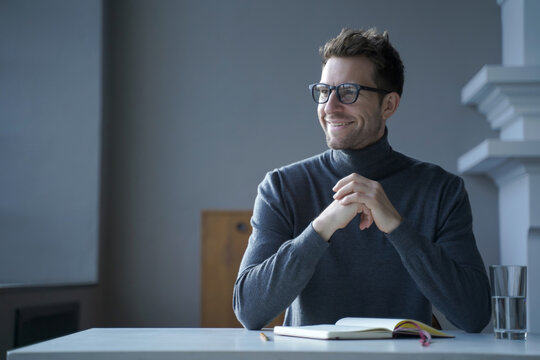 Smiling man with glasses sitting at table with notebook in home office