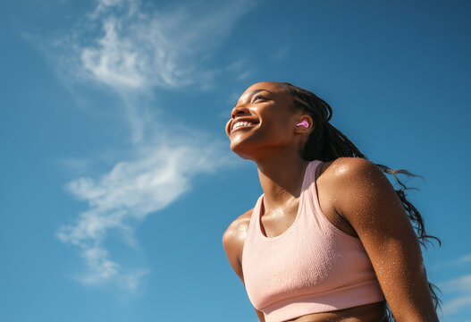 Un vibrante momento de ejercicio al aire libre que captura energ&iacute;a, confianza y bienestar moderno bajo un cielo azul brillante e inspirador. Una mujer atl&eacute;tica con ropa deportiva rosa y auriculares 
