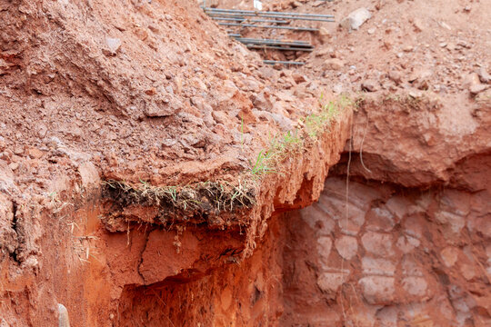 Excavation in red soil with ground cutting for foundation preparation at a construction site.