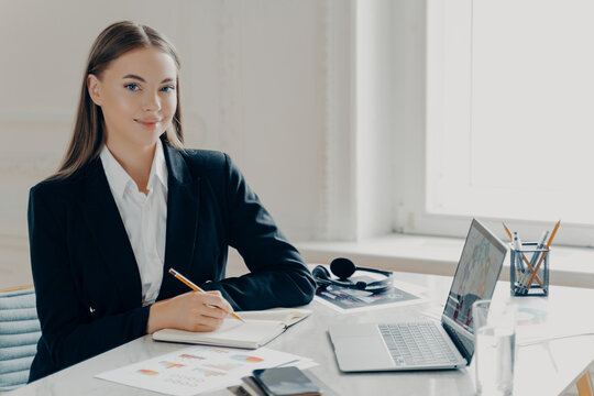 Business woman working on laptop and writing notes at office desk