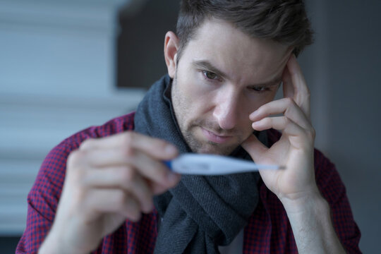 Sick man checking thermometer at home with worried expression