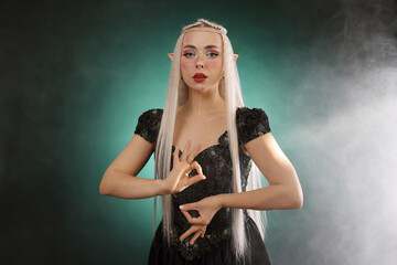 Naklejka premium Beautiful girl dressed as elf on dark background with smoke