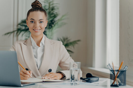 Smiling business woman writing notes at office desk with laptop