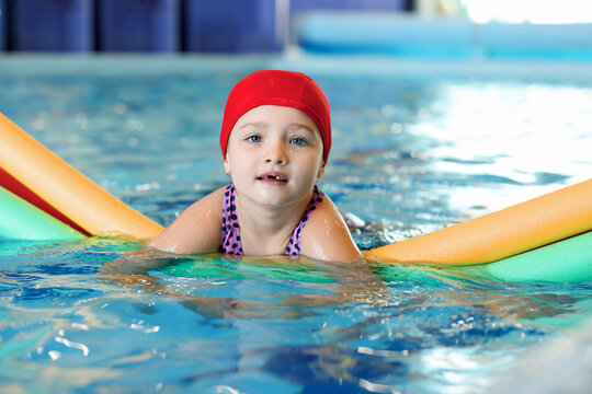 Cute little girl swimming with water noodles during lesson in pool