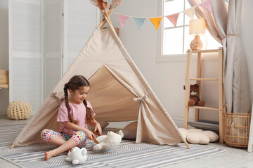 Little girl playing with toys near toy wigwam in playroom, space for text © New Africa