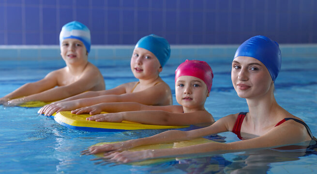 Coach teaching little kids to swim with kickboards in pool