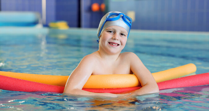Cute little boy swimming with water noodles during lesson in pool