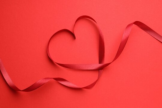 Heart made of ribbon on red background, top view
