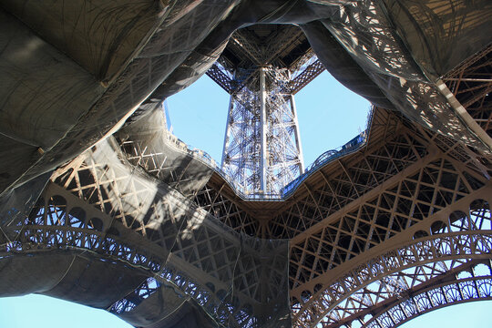 Intricate geometric view of the Eiffel Tower's iron lattice from below. Abstract architectural photography of the famous Paris landmark against a clear blue sky.