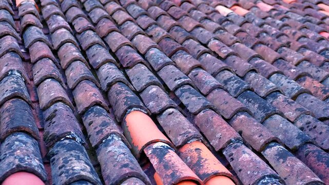 Old terracotta clay roof tiles pattern. Detailed view of weathered, rustic clay roof tiles creating a traditional architectural pattern with a mixture of old dark and new red terracotta shingles