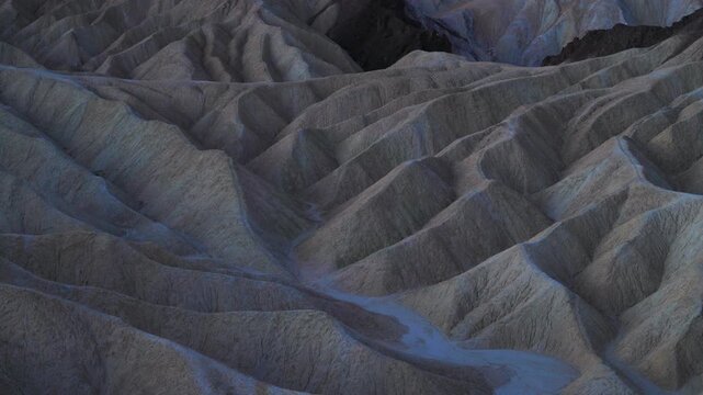Dramatic Zabriskie Point in Death Valley landscape reveals intricate ridge patterns and deep ravines. Sedimentary rock formations create flowing textures across the barren desert terrain.