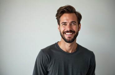 Obraz premium Happy man with beard smiles broadly, looking at camera. Casual guy wears dark t-shirt against plain background. Copy space available for text overlay.