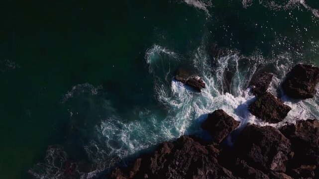 Aerial view of waves crashing on rugged rocky coastline.