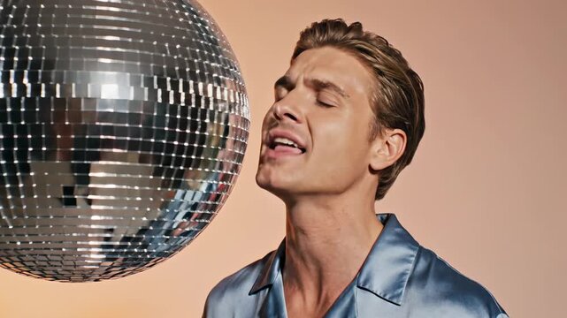 This features a man in a shiny blue shirt looking up at a large disco ball, capturing the essence of a retro party atmosphere with a sense of fun and celebration.