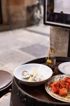 oysters with lemon, tomato salad, glass of vermouth, outdoor dining in spain on barrel tabletop with street in the background
