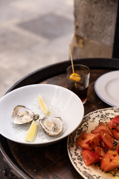 oysters with lemon, tomato salad, glass of vermouth, outdoor dining in spain on barrel tabletop with street in the background