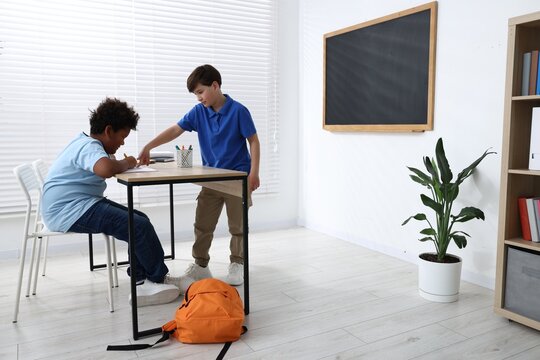 Boy bullying his African American classmate in classroom, space for text