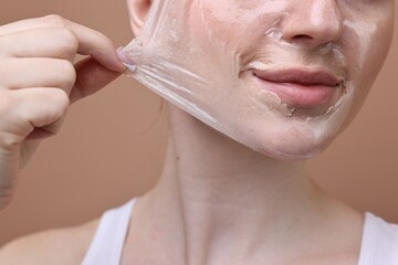 Beautiful woman peeling off facial mask on brown background, closeup