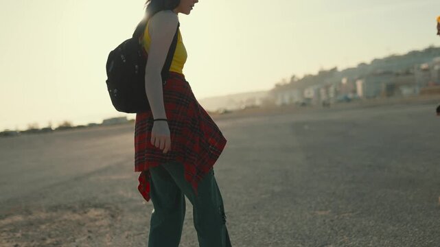 Young woman longboarding at sunset on asphalt