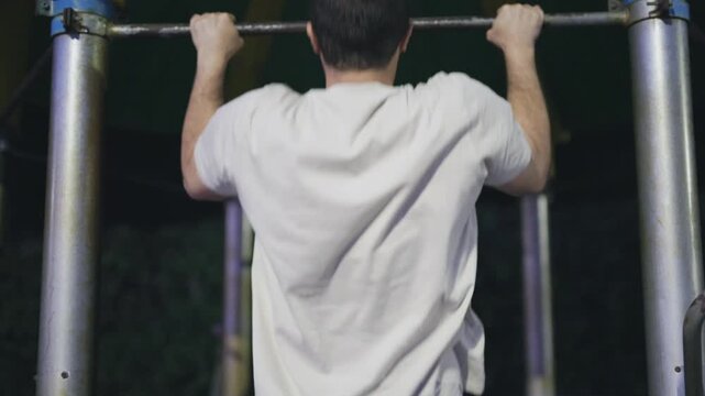 Athletic man doing pull-ups outdoors at night