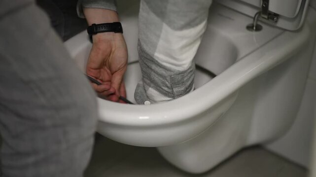 Plumber wearing gloves using a plumbing snake to clear a blockage inside a toilet bowl