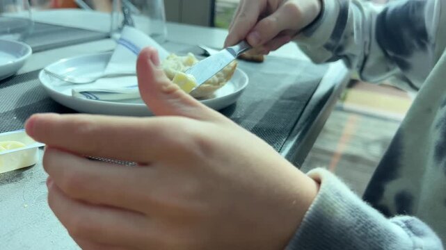 Spreading butter on bread at dining table, close up meal scene