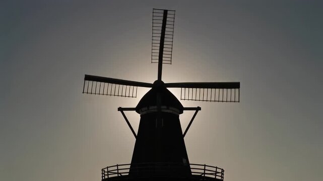 Silhouette of a traditional Dutch windmill against a clear sky during sunset, showcasing its iconic design and rural charm