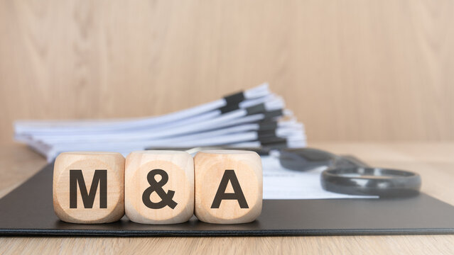 M and A text on wooden blocks with business documents.