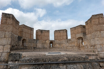 Fototapeta premium Detailed view of the medieval stone battlements and ramparts of Peñafiel Castle in Valladolid, Spain. The ancient fortress defenses show distinct merlons and arrow slits under a cloudy blue sky.