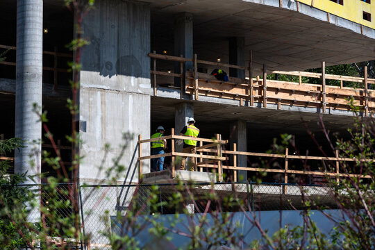 Construction workers in safety vests and hard hats standing on concrete floor of new build residential real estate development, condominium or apartment building, no walls, safety railings
