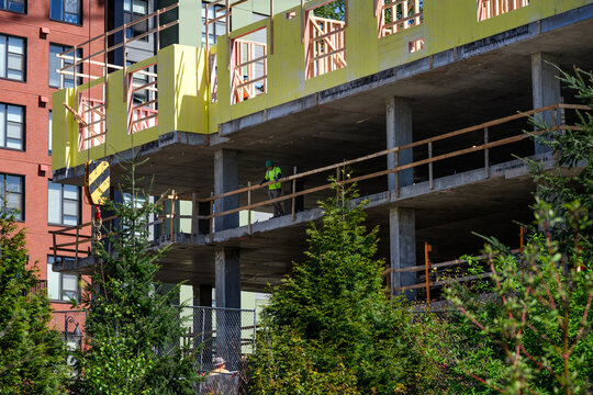 Construction worker standing at railing on concrete floor of new residential high rise building, new real estate development, wood framing and external sheathing
