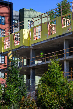 Construction worker standing at railing on concrete floor of new residential high rise building, new real estate development, wood framing and external sheathing
