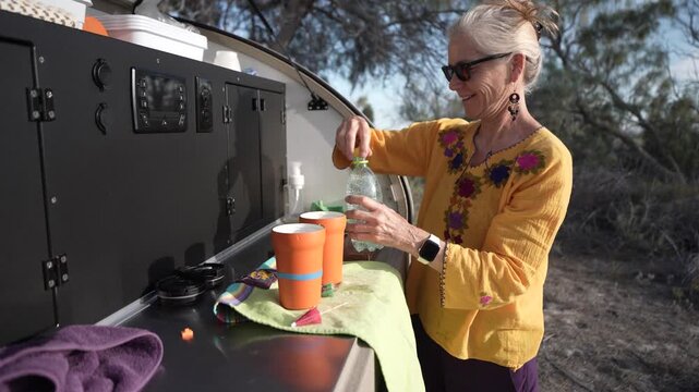 Mature woman prepares drinks with care in her teardrop camper trailer while enjoying her time in Baja California Mexico.