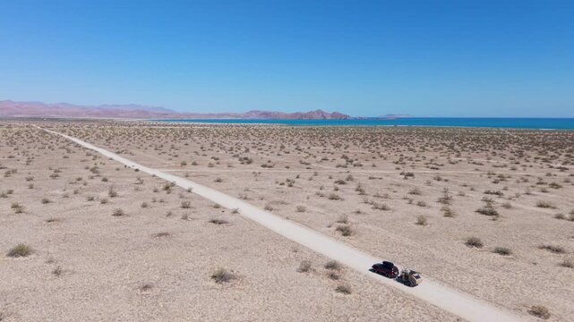 SUV drives on dirt roads pulling a teardrop camper trailer next to the ocean on a camping trip in Baja California Mexico.