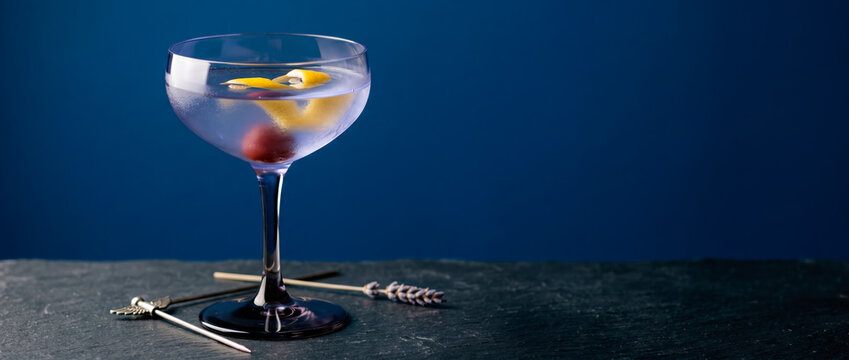 Elegant purple cocktail garnished with lemon twist and cherry served in coupe glass on dark slate with lavender sprig and garnish pick for sophisticated bar or party enjoyment occasions