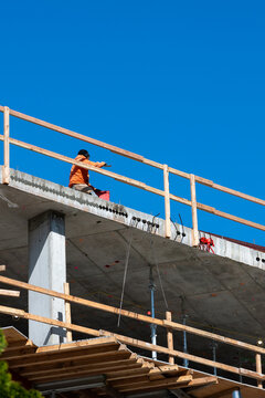 Construction worker high up on building project working on grouting structural post-tensioning wire strand holes running through concrete slab of floor
