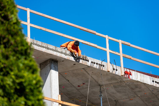 Construction worker high up on building project working on grouting structural post-tensioning wire strand holes running through concrete slab of floor
