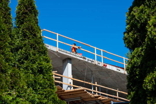 Construction worker high up on building project working on grouting structural post-tensioning wire strand holes running through concrete slab of floor
