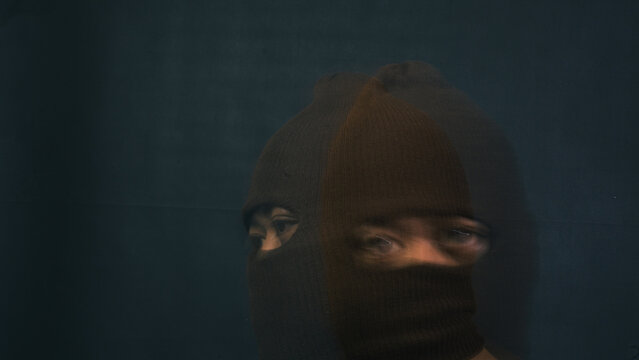 A mysterious male wearing a dark brown knitted balaclava is captured in a tight overlapping double exposure effect that shifts his face slightly. The disorienting and still ghosting