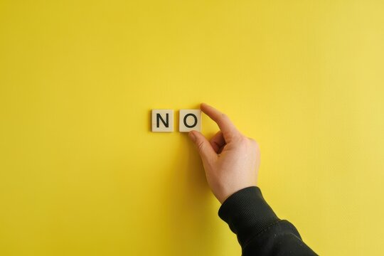 A hand placing a wooden tile letter O next to letter N on yellow background