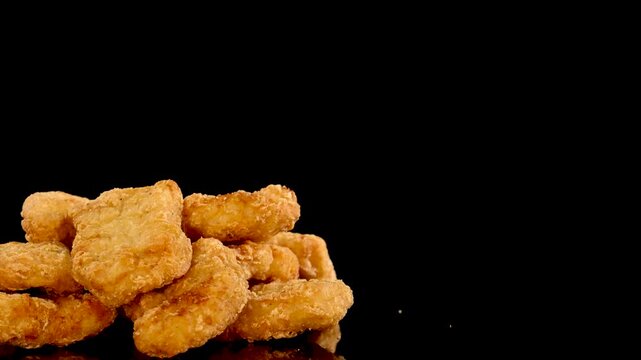 Pile of golden chicken nuggets rotating on black background with reflection.