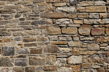 Fototapeta premium Rough stone wall with varied sizes and natural hues. Stones form a sturdy, weathered surface. Textures show age and craftsmanship. Ideal for architectural backgrounds or historical contexts